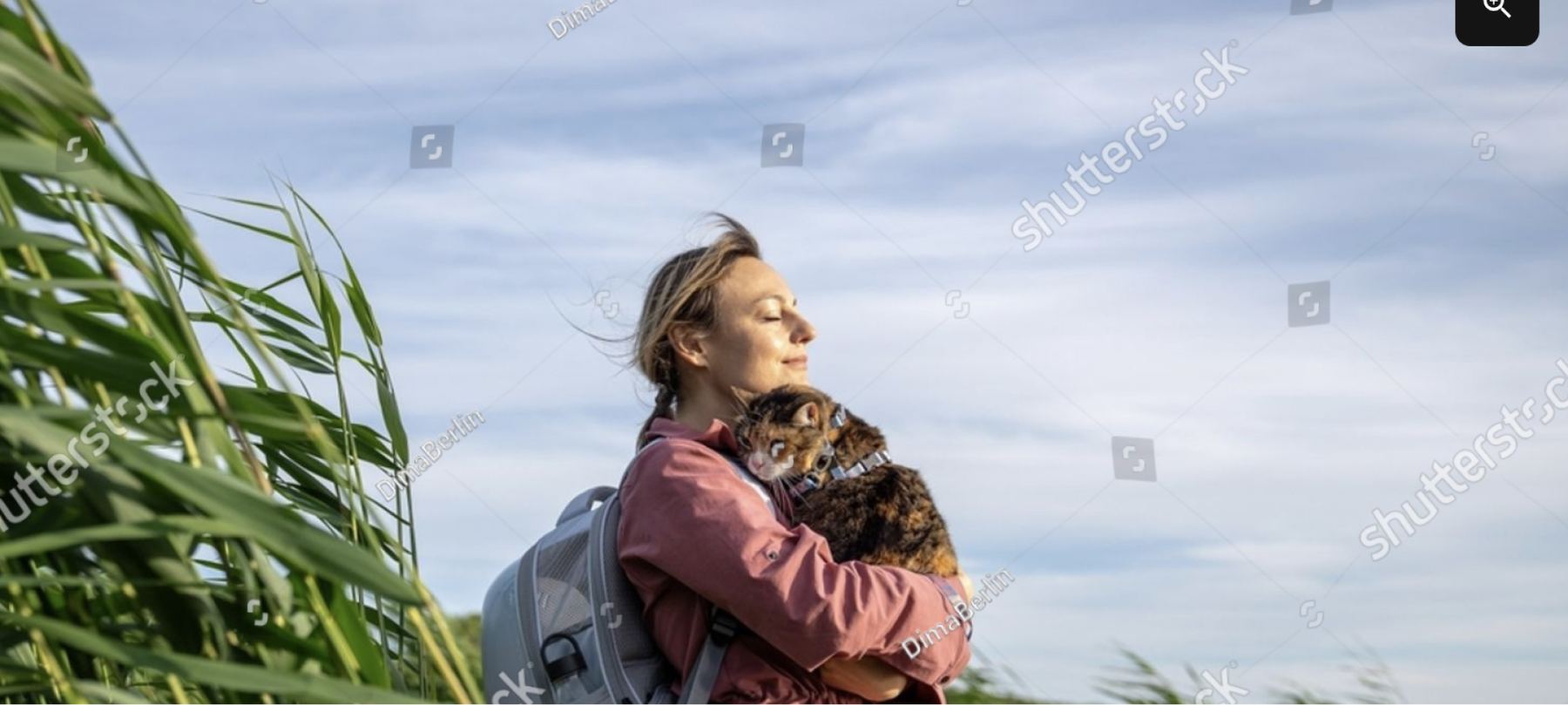 A woman standing in the coastal grass, hugging her tabby cat
